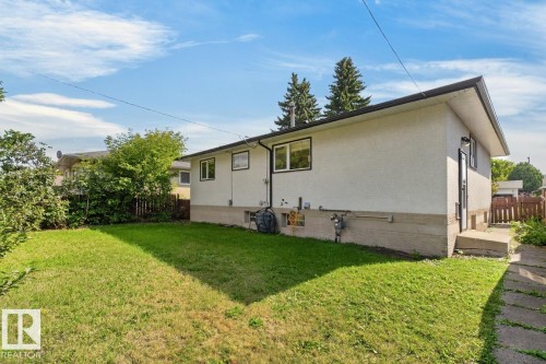Expansive rear yard featuring green lawn, mature trees, and a concrete pathway - 7304 98A Avenue Nw, Edmonton, AB 
