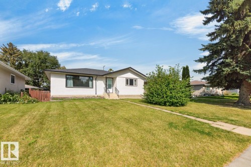 White exterior with dark trim windows, front entry with steps and handrails, mature landscaping, and a manicured lawn - 7304 98A Avenue Nw, Edmonton, AB 
