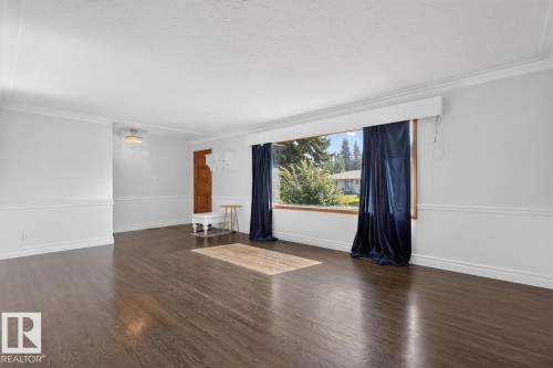 Dark wood-finish flooring, white walls with wainscoting, crown molding, a large window with wood trim, and a decorative ceiling light fixture - 7304 98A Avenue Nw, Edmonton, AB 