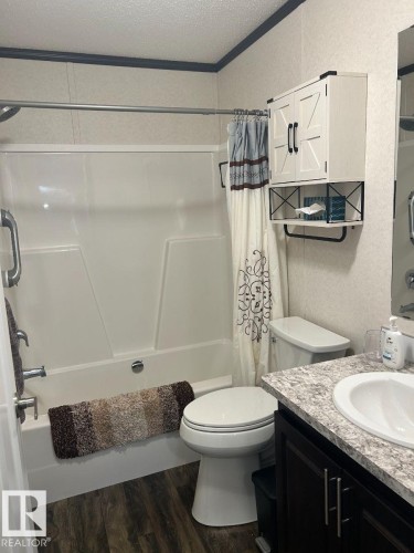 Tub/shower combination with a shower rod, dark wood-finish vanity with a white basin, light-toned countertop, and wood-finish flooring - 63 Willow Park Estates, Leduc, AB 