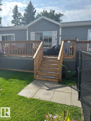 Rear exterior featuring grey siding, a wood-finish deck with railings, and stairs leading to a concrete patio - 63 Willow Park Estates, Leduc, AB 