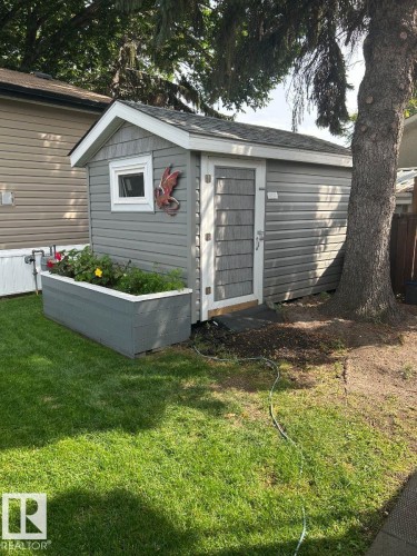 Utility shed featuring horizontal siding, a shingled roof, a single window, and a planted raised garden bed - 63 Willow Park Estates, Leduc, AB 