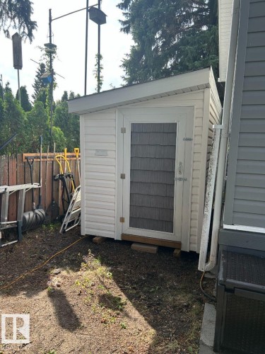 White vinyl siding shed with shingle-style door panel, featuring a white trim door frame and sloped roof - 63 Willow Park Estates, Leduc, AB 