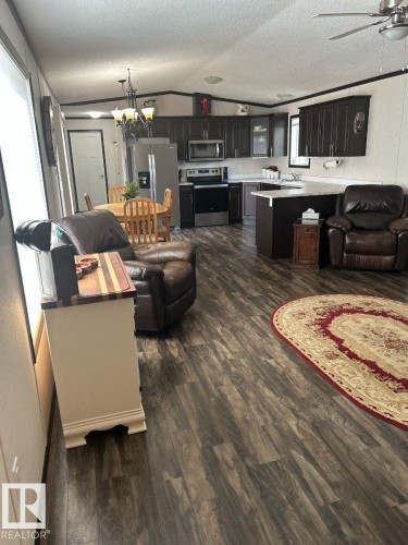 Open-concept kitchen and living area featuring dark wood-finish cabinetry, stainless steel appliances, and wood-finish flooring - 63 Willow Park Estates, Leduc, AB 