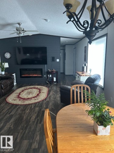 Open-concept living area with dark wood-finish flooring, a contemporary electric fireplace, and a ceiling fan - 63 Willow Park Estates, Leduc, AB 