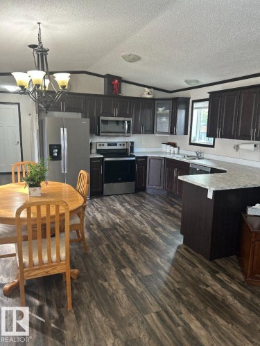Kitchen featuring rich wood-finish cabinetry, stainless steel appliances, light-toned countertops, wood-finish flooring, and a ceiling-mounted chandelier - 63 Willow Park Estates, Leduc, AB 