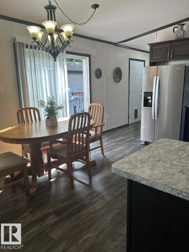 Wood-finish flooring, sliding glass door, overhead chandelier, dark wood-finish cabinetry, and stainless steel refrigerator - 63 Willow Park Estates, Leduc, AB 