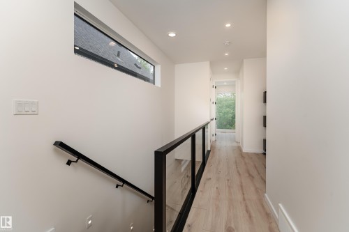Wood-finish flooring with recessed lighting, linear transom window, and a glass panel railing with a black metal frame - 10138 90 Street Nw, Edmonton, AB 