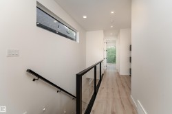 Wood-finish flooring with recessed lighting, linear transom window, and a glass panel railing with a black metal frame - 