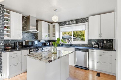 White cabinetry with modern hardware, stone countertops, stainless steel appliances, a center island with a stone surface, and wood-finish flooring - 3523 106 Street Nw, Edmonton, AB 