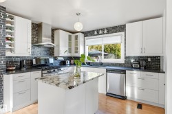White cabinetry with modern hardware, stone countertops, stainless steel appliances, a center island with a stone surface, and wood-finish flooring - 