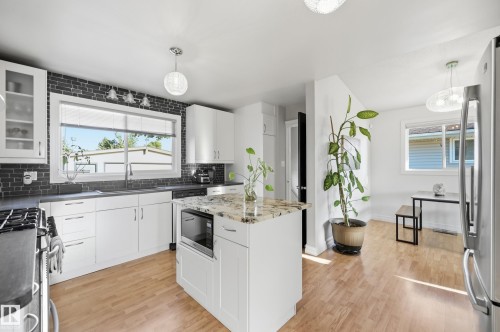 White cabinetry, granite-finish island countertop, dark brick-style backsplash, stainless steel appliances, and wood-finish flooring - 3523 106 Street Nw, Edmonton, AB 