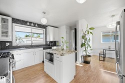 White cabinetry, granite-finish island countertop, dark brick-style backsplash, stainless steel appliances, and wood-finish flooring - 