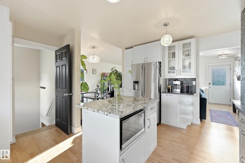 Kitchen featuring white cabinetry, a kitchen island with built-in microwave, stainless steel refrigerator, and wood-finish flooring - 3523 106 Street Nw, Edmonton, AB 