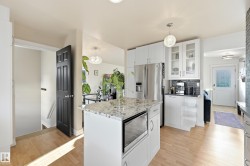 Kitchen featuring white cabinetry, a kitchen island with built-in microwave, stainless steel refrigerator, and wood-finish flooring - 