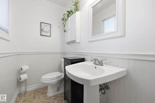 Pedestal sink with chrome faucet, white beadboard wainscoting, wall-mounted mirror, and tile flooring - 3523 106 Street Nw, Edmonton, AB 