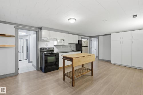 Light wood-finish flooring throughout, white upper and lower cabinetry, white subway tile backsplash, and a black built-in range - 3523 106 Street Nw, Edmonton, AB 