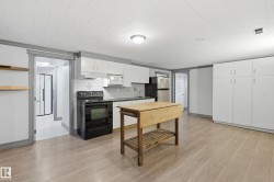 Light wood-finish flooring throughout, white upper and lower cabinetry, white subway tile backsplash, and a black built-in range - 