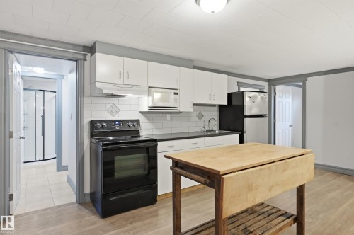 Kitchen featuring white upper and lower cabinetry, subway tile backsplash, and wood-finish flooring - 3523 106 Street Nw, Edmonton, AB 