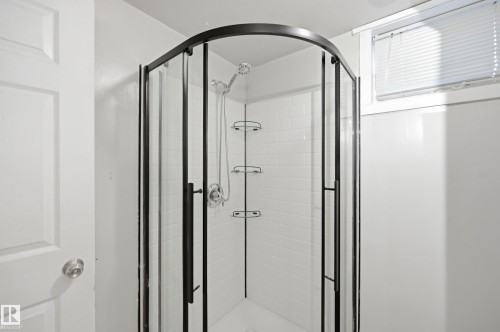Curved glass shower enclosure with black framing, white subway tile surround, and built-in shower shelving - 3523 106 Street Nw, Edmonton, AB 