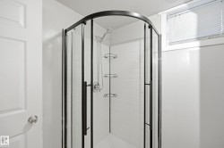 Curved glass shower enclosure with black framing, white subway tile surround, and built-in shower shelving - 