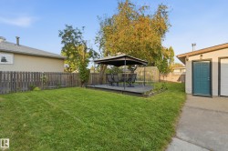 Expansive backyard featuring a large green space, privacy fencing, a wood-finish deck, and a greenhouse structure - 