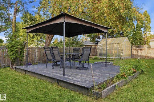 Expansive backyard featuring a wood deck, a covered patio area, a greenhouse structure, a fire pit, and defined garden beds - 3523 106 Street Nw, Edmonton, AB 