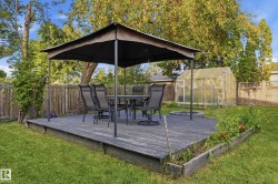 Expansive backyard featuring a wood deck, a covered patio area, a greenhouse structure, a fire pit, and defined garden beds - 