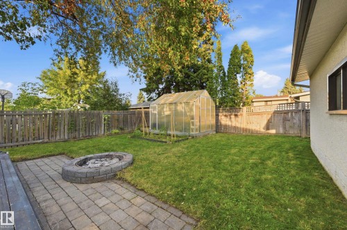 Expansive backyard featuring a manicured lawn, a built-in greenhouse, a stone-paved patio, and a stone fire pit - 3523 106 Street Nw, Edmonton, AB 