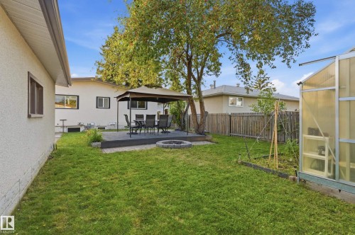 Expansive backyard featuring a manicured lawn, a raised patio with a gazebo, a circular fire pit, and a greenhouse structure - 3523 106 Street Nw, Edmonton, AB 