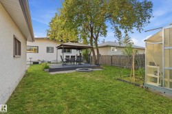 Expansive backyard featuring a manicured lawn, a raised patio with a gazebo, a circular fire pit, and a greenhouse structure - 