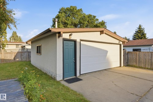 Detached garage with a white overhead door, a teal side entry door, an exterior wall sconce, and a side window - 3523 106 Street Nw, Edmonton, AB 