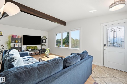 Vaulted ceiling with exposed wood beam, wood-finish flooring, windows with white trim, white entry door with decorative glass inlay, and irregular-patterned tile entry - 3523 106 Street Nw, Edmonton, AB 