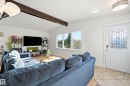 Vaulted ceiling with exposed wood beam, wood-finish flooring, windows with white trim, white entry door with decorative glass inlay, and irregular-patterned tile entry - 3523 106 Street Nw, Edmonton, AB 