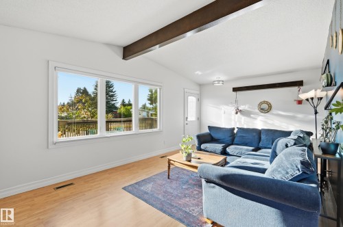 Vaulted ceiling with exposed beams, wood-finish flooring, white trim, and a large window - 3523 106 Street Nw, Edmonton, AB 