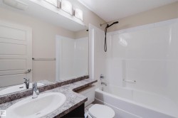 Bathroom featuring a white drop-in sink with a chrome faucet, a speckled countertop, an oversized wall mirror, and a full bathtub with an integrated shower and black showerhead - 