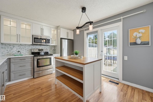 Stainless steel appliances, two-tone cabinetry, wood-finish flooring, glass-paneled patio door, and a kitchen island with open shelving - 4125 38 Street Nw, Edmonton, AB 