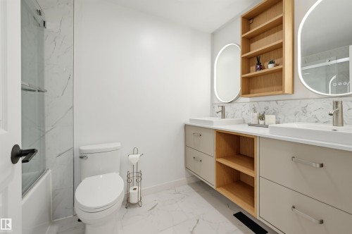 Dual vessel sinks with wall-mounted faucets, illuminated oval mirrors, and a built-in wood-finish shelving unit - 4125 38 Street Nw, Edmonton, AB 
