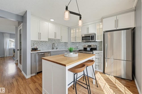 Kitchen featuring stainless steel appliances, mosaic tile backsplash, white upper and grey lower cabinetry, and a wood-finish island countertop - 4125 38 Street Nw, Edmonton, AB 