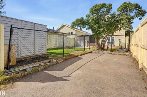 Paved outdoor area featuring perimeter fencing, an enclosed storage structure, and mature trees - 4125 38 Street Nw, Edmonton, AB 