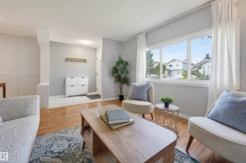 Spacious living area featuring light wood-finish flooring, a large multi-pane window, and a decorative paneled wall detail - 4125 38 Street Nw, Edmonton, AB 