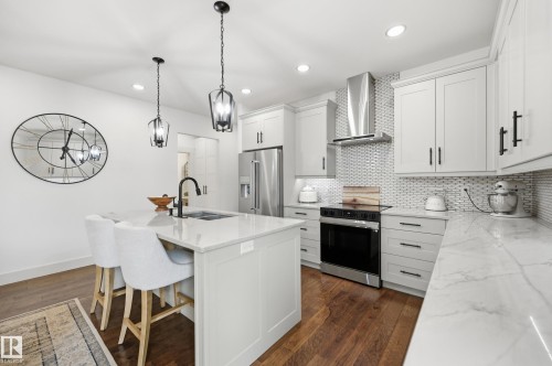 Kitchen featuring light cabinetry, stainless steel appliances, wood-finish flooring, a central island with a sink, and pendant lighting - 1961 Adamson Terrace Sw, Edmonton, AB 
