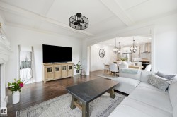 White coffered ceiling, dark wood-finish flooring, and an arched doorway leading to a dining area with pendant lighting and a kitchen - 