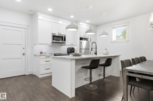 Modern kitchen featuring white cabinetry, stainless steel appliances, a center island with countertop seating, and wood-finish flooring - 1961 Adamson Terrace Sw, Edmonton, AB 