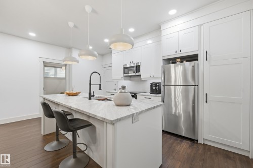 Kitchen featuring a central island with a sink, white cabinetry, stainless steel appliances, dark wood-finish flooring, and recessed lighting - 1961 Adamson Terrace Sw, Edmonton, AB 