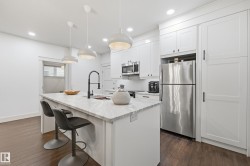 Kitchen featuring a central island with a sink, white cabinetry, stainless steel appliances, dark wood-finish flooring, and recessed lighting - 