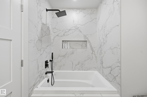 Bathtub with integrated shelving, matte black fixtures, and full-height marbled wall tiling - 1961 Adamson Terrace Sw, Edmonton, AB 