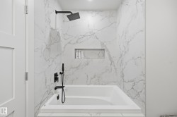 Bathtub with integrated shelving, matte black fixtures, and full-height marbled wall tiling - 