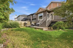 Expansive grassy area with mature foliage, a raised wooden deck, and a lower wooden patio - 