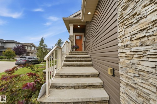 Exterior featuring stacked stone accents, horizontal siding, concrete steps with stone risers, and a prominent front entrance with a wooden door - 1961 Adamson Terrace Sw, Edmonton, AB 